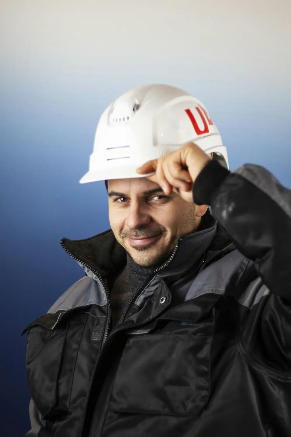 a man wearing a white hard hat and black jacket
